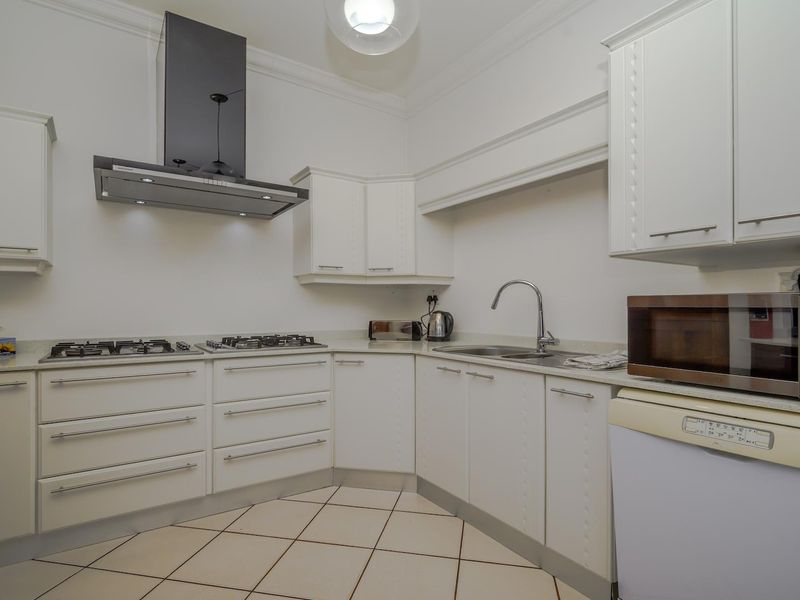 A functional kitchen featuring white cabinetry, a gas hob with extractor fan, stainless steel sink, and tiled flooring.