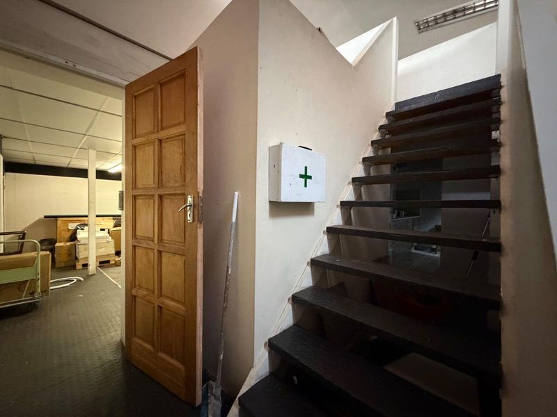 A functional hallway area featuring a wooden staircase, a wall-mounted first aid cabinet, and access to an adjacent storage or utility space.