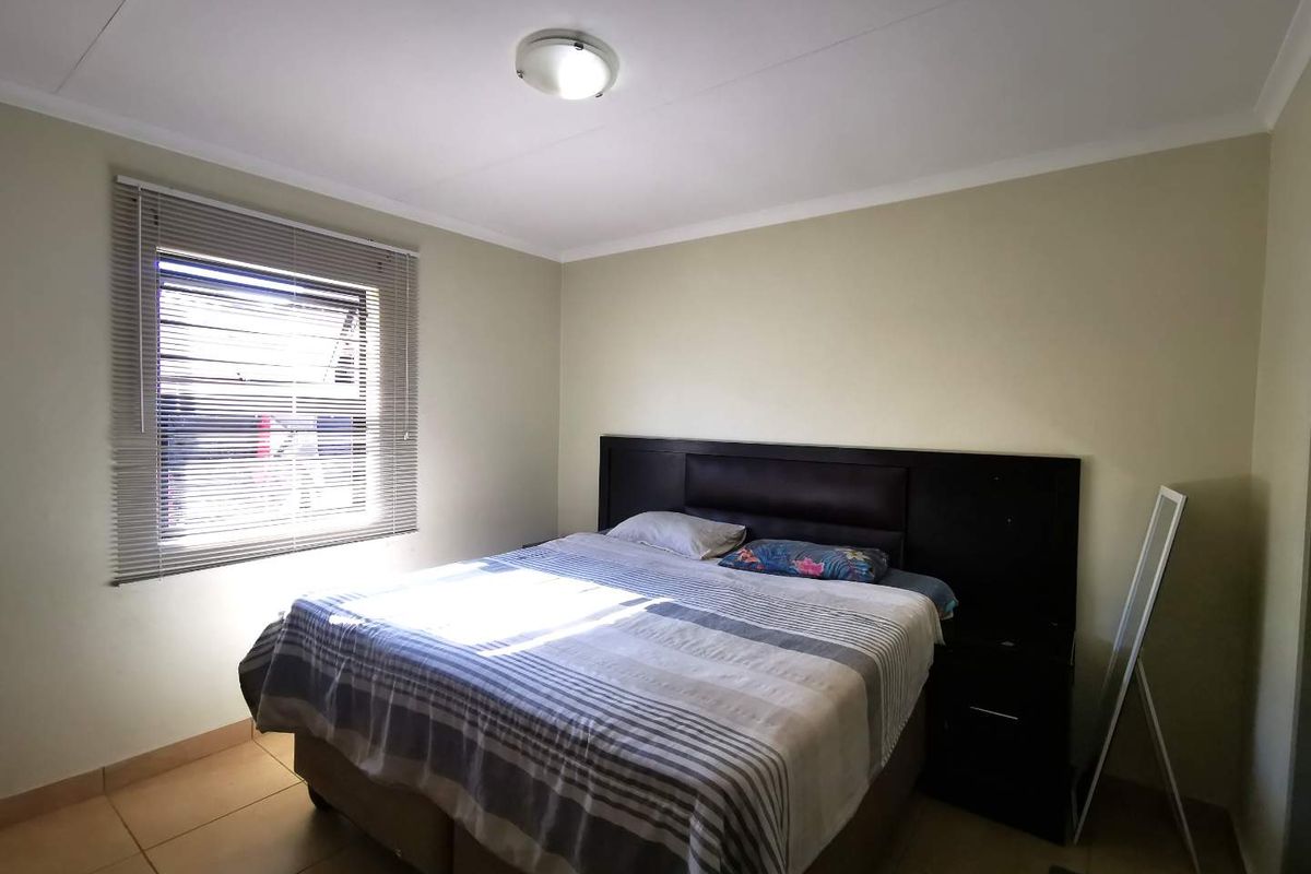 A functional bedroom featuring tiled flooring, a window with fitted blinds, and a ceiling-mounted light fixture.