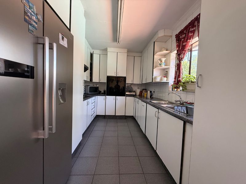 A functional galley-style kitchen featuring white cabinetry, tiled flooring, a double sink, and a built-in oven, offering a practical layout for daily meal preparation.