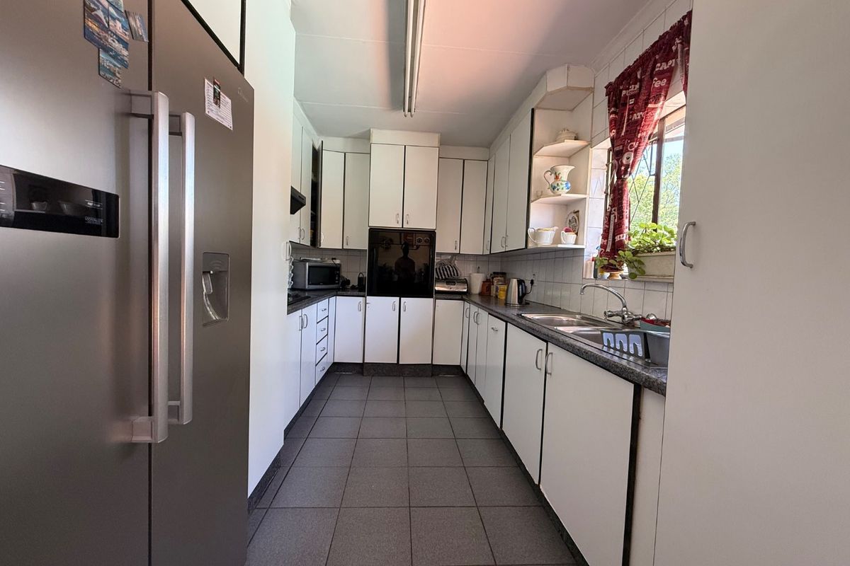 A functional galley-style kitchen featuring white cabinetry, tiled flooring, a double sink, and a built-in oven, offering a practical layout for daily meal preparation.