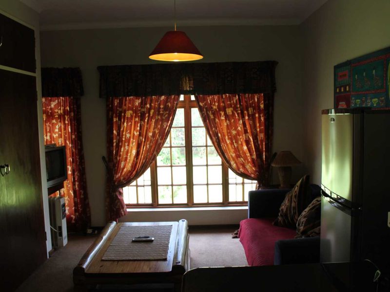 A living room featuring a large timber-framed window, built-in storage cabinetry, and carpeted flooring, offering a cozy and traditional cottage aesthetic.