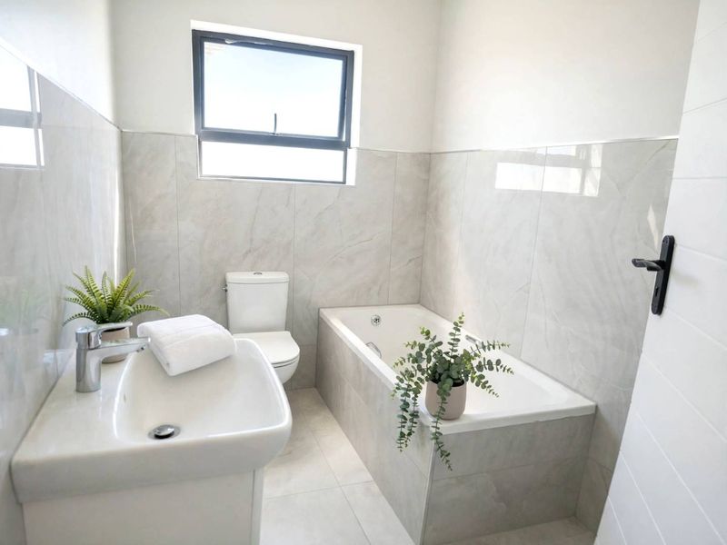 A modern, well-maintained bathroom featuring neutral large-format wall and floor tiles, a built-in bathtub, and a contemporary vanity basin.