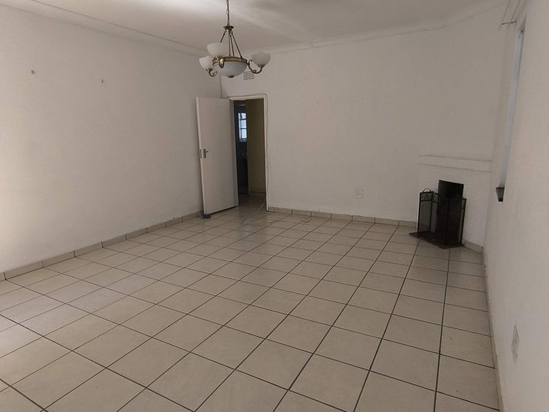 A spacious, empty living room featuring neutral tiled flooring, a built-in fireplace, and classic ceiling detailing, offering a blank canvas for interior design.