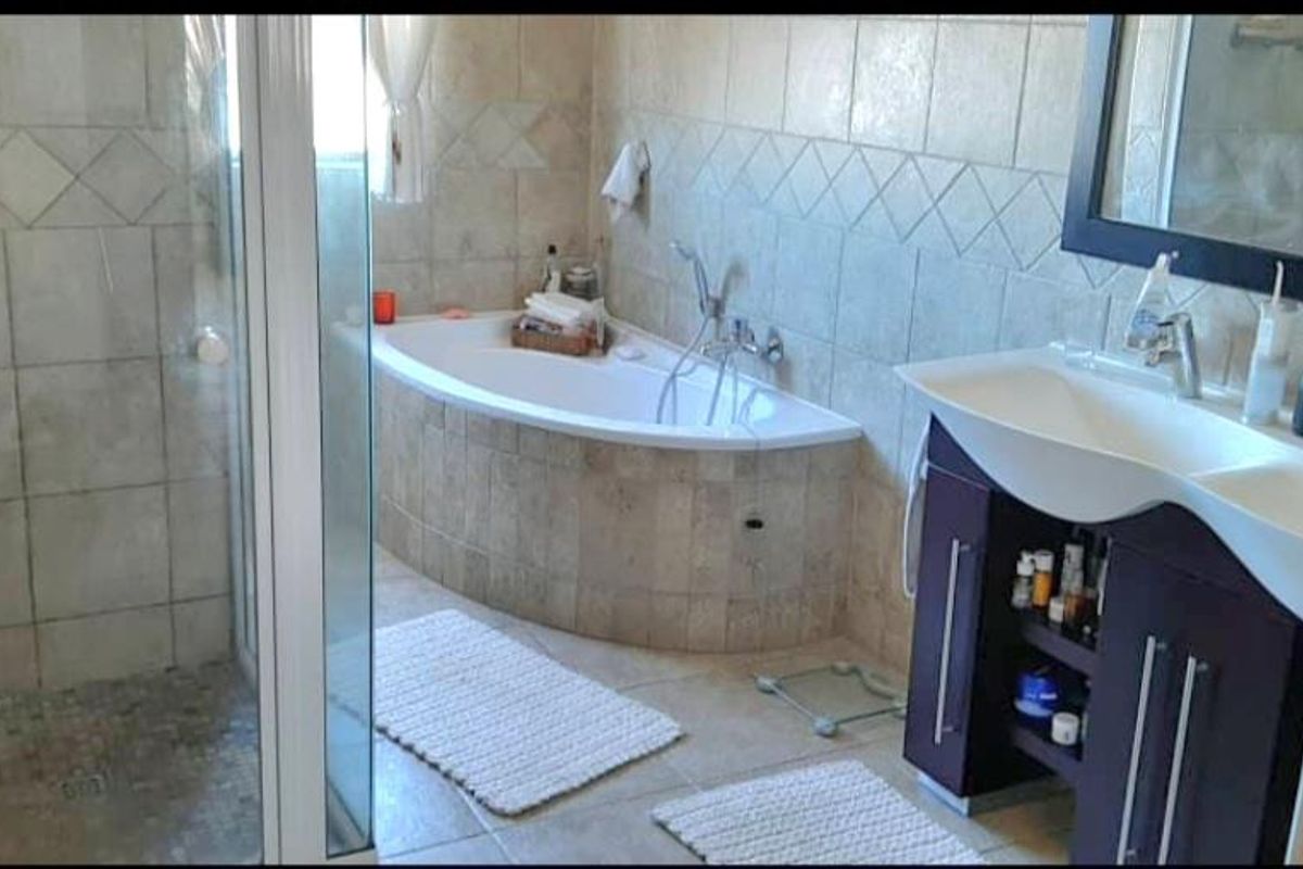A functional bathroom featuring a tiled shower enclosure, a built-in bathtub with stone-look tiling, and a modern vanity unit with a basin.