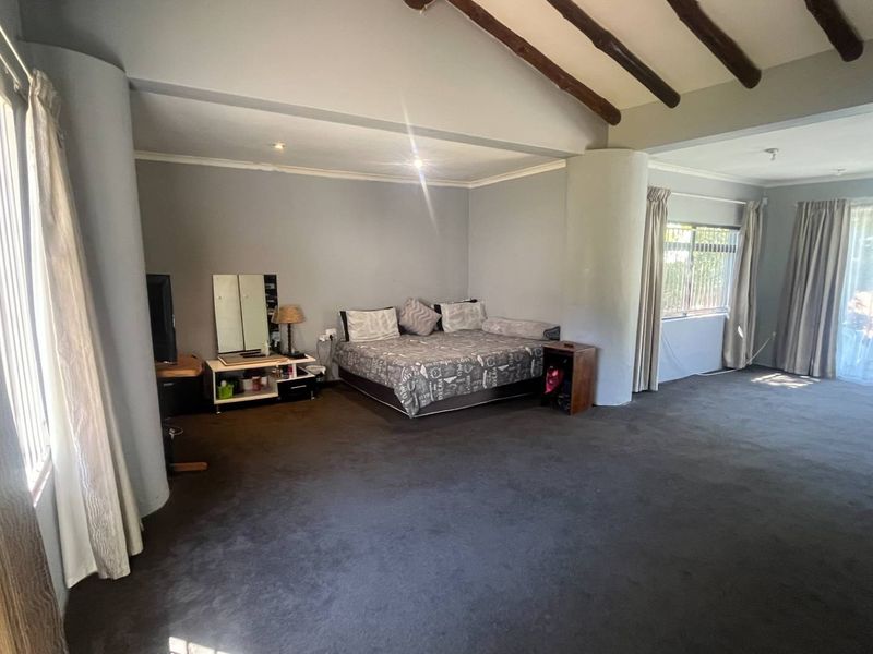 Spacious bedroom featuring a vaulted ceiling with exposed timber beams, neutral wall finishes, and direct access to the outdoors via sliding glass doors.