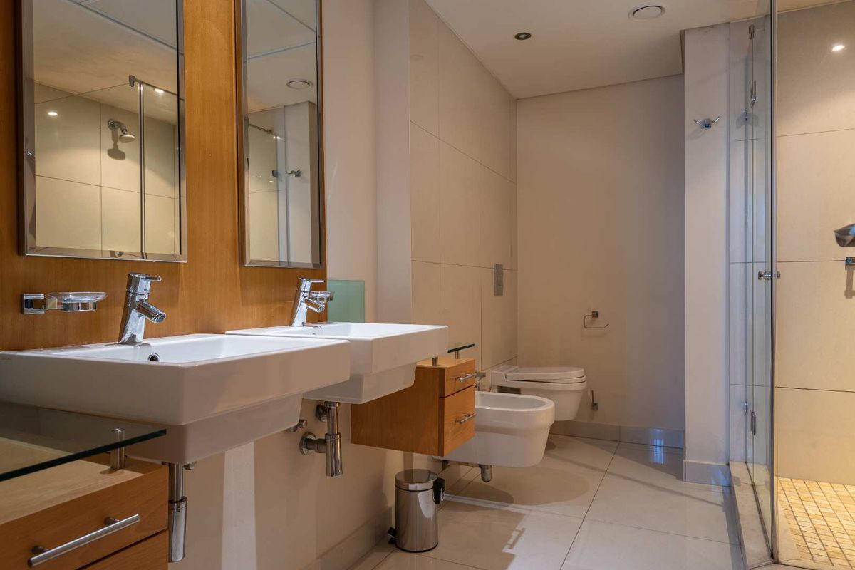 Modern bathroom featuring a double vanity with wall-mounted basins, a bidet, a wall-hung toilet, and a glass-enclosed walk-in shower with tiled flooring.