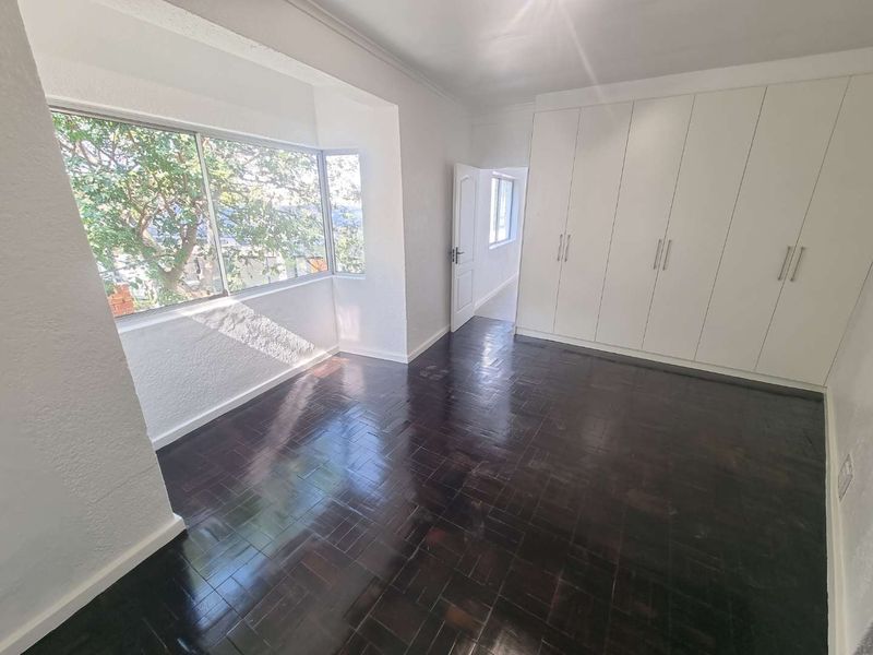 A bright, empty bedroom featuring polished dark parquet flooring and extensive built-in white cupboards, offering ample storage space and natural light.