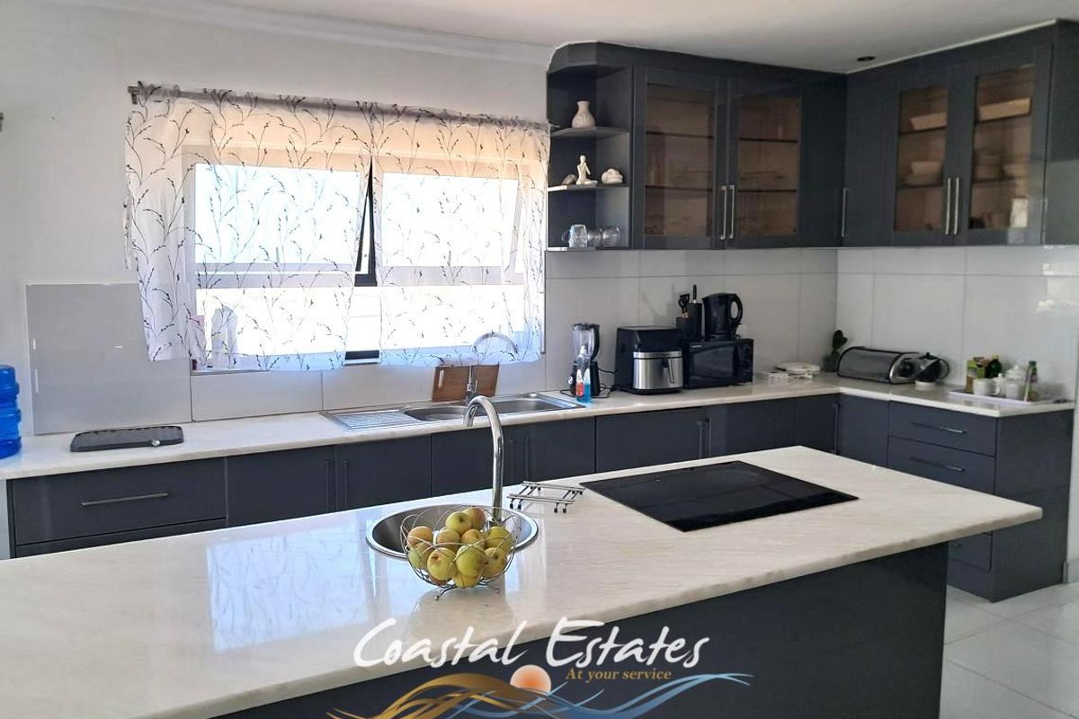 Modern kitchen featuring dark grey cabinetry, stone countertops, a central island with an integrated induction hob, and a double sink.