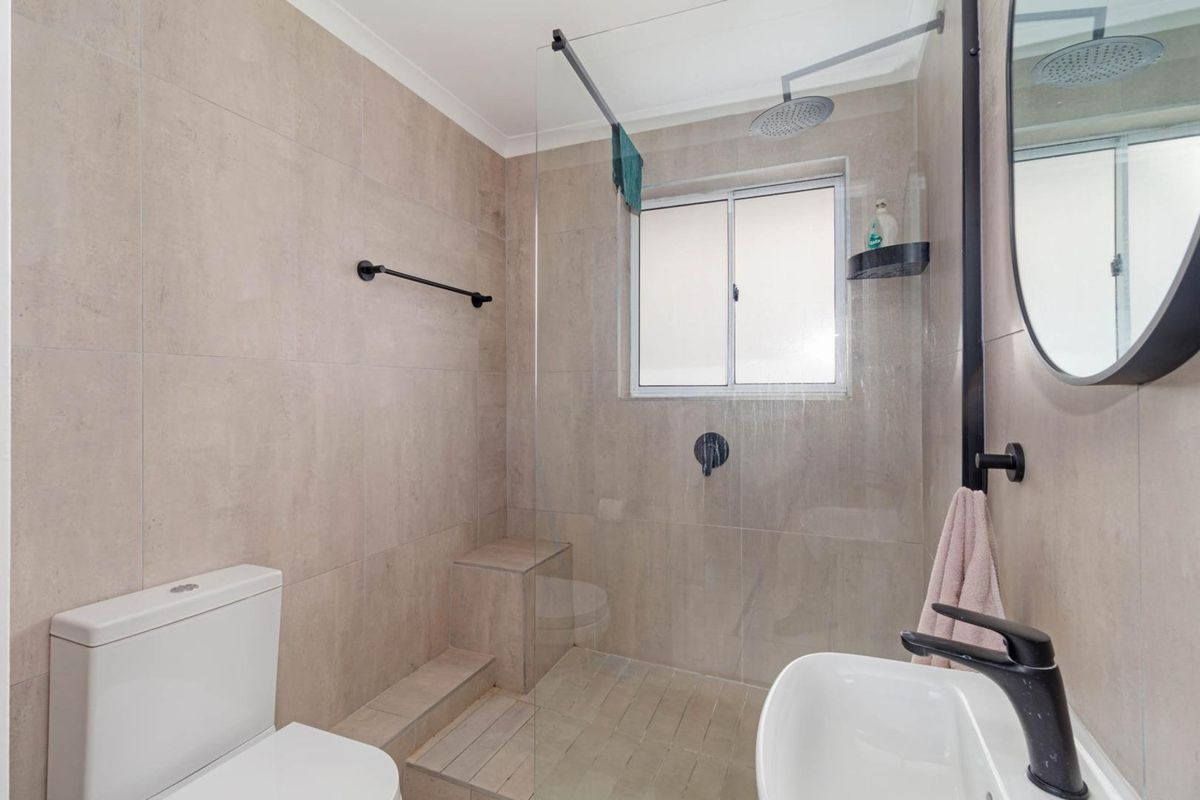 Modern bathroom featuring a walk-in shower with a glass screen, rainfall showerhead, built-in tiled bench, and contemporary black fixtures.