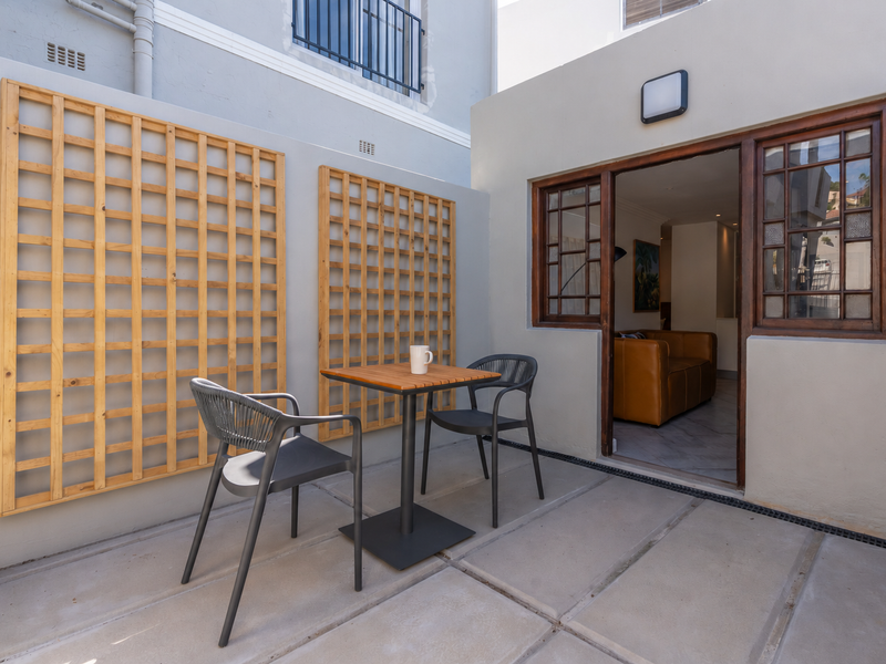 A private paved patio area featuring timber wall trellises and direct access to the interior living space through a timber-framed glass door.