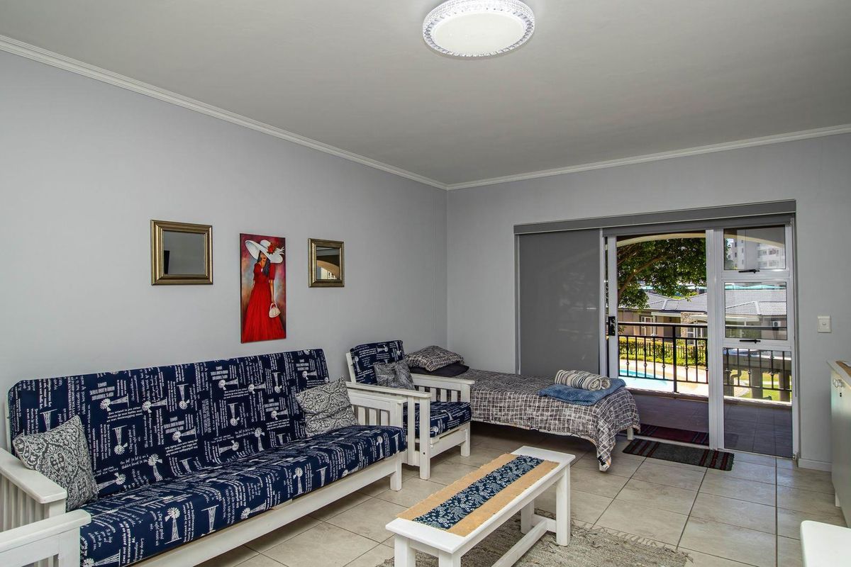 A living area featuring tiled flooring and sliding glass doors that open onto a balcony with views of the complex pool.