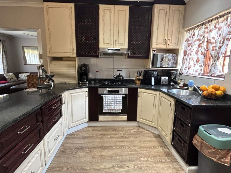 A functional kitchen featuring two-tone cabinetry, granite countertops, a gas hob, and an integrated oven, with a view into the adjacent living area.