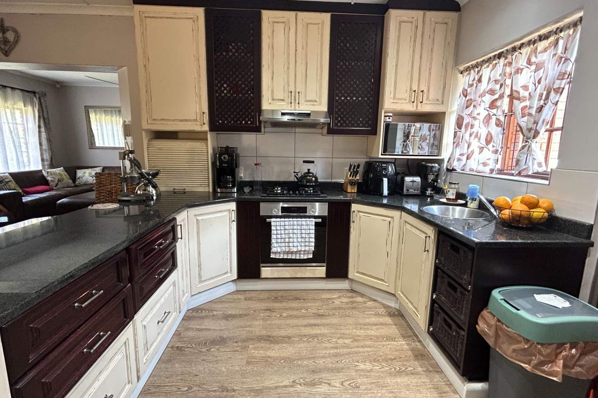 A functional kitchen featuring two-tone cabinetry, granite countertops, a gas hob, and an integrated oven, with a view into the adjacent living area.