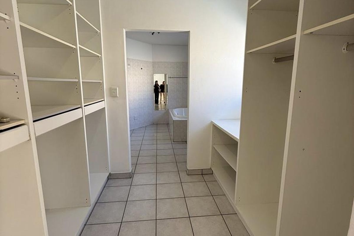 A walk-in dressing area featuring extensive built-in white cabinetry and tiled flooring, leading directly into an adjoining bathroom space.