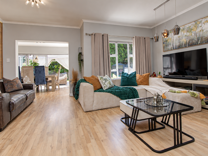 Spacious open-plan living area featuring light laminate flooring, a timber accent wall, and seamless flow to an adjoining dining space and patio.