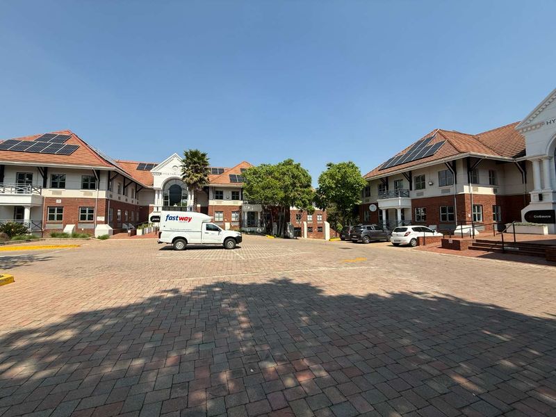 A well-maintained office park complex featuring brick facades, tiled roofing with solar installations, and extensive paved parking areas.