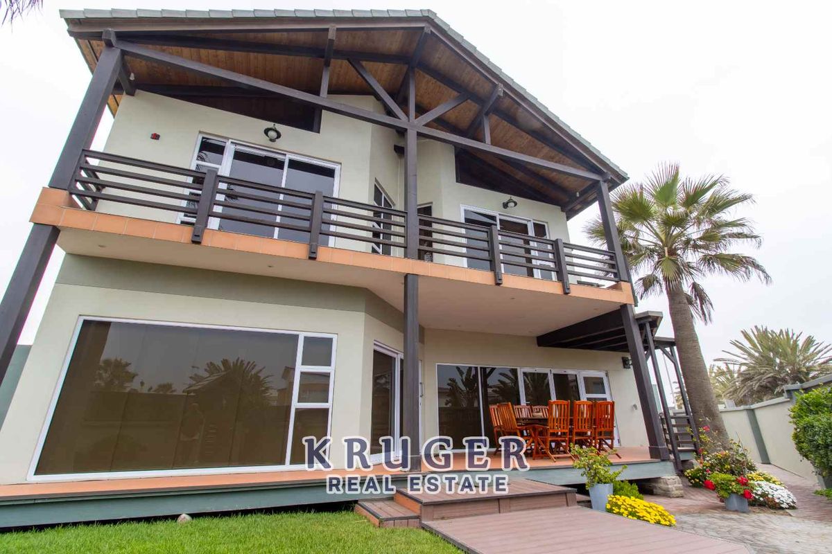 A two-story residential property featuring a rear patio, timber-framed balcony, large glass sliding doors, and a pitched roof design.