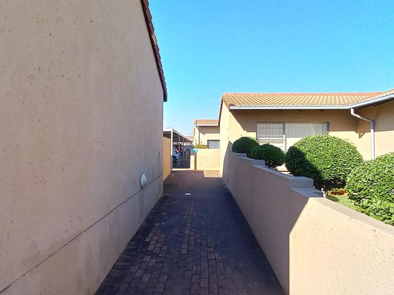 A paved walkway leading between townhouse units, featuring boundary walls and established shrubbery.