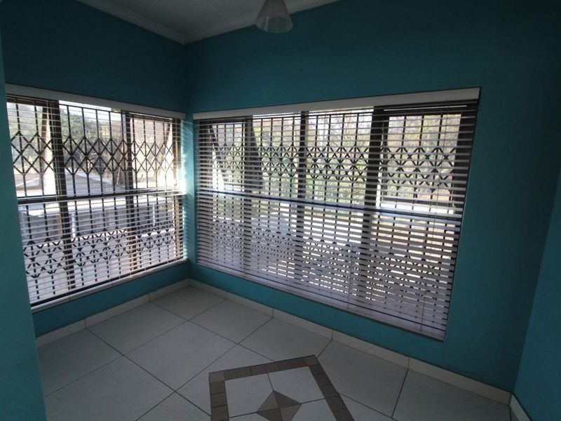 A bright, empty living area featuring tiled flooring, large windows with fitted venetian blinds, and integrated security gates for added protection.