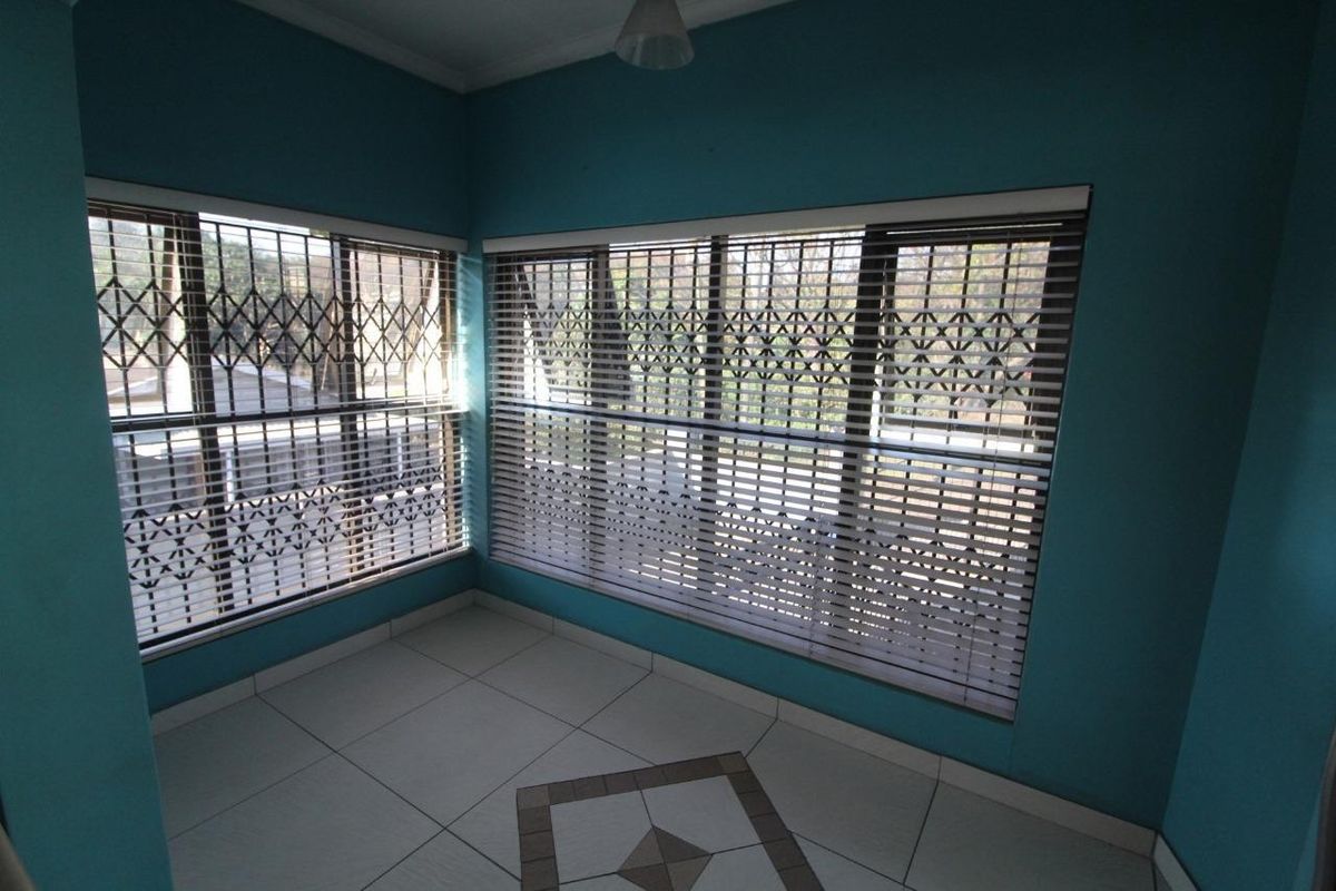 A bright, empty living area featuring tiled flooring, large windows with fitted venetian blinds, and integrated security gates for added protection.