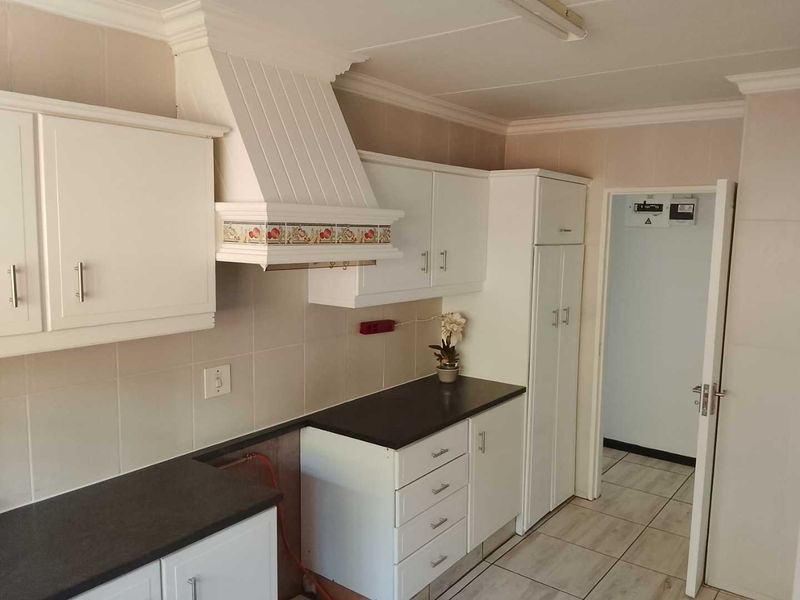 A functional kitchen featuring white cabinetry, dark countertops, tiled backsplash, and a built-in extractor fan, with space prepared for a stove installation.