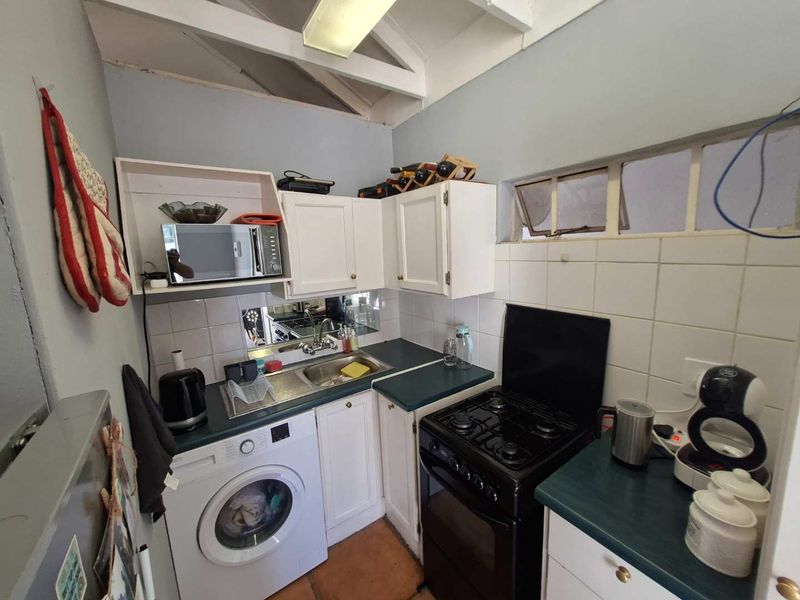Compact kitchen featuring white cabinetry, laminate countertops, tiled backsplash, and exposed rafters, with integrated laundry and cooking facilities.