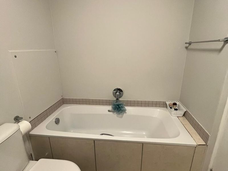 A functional bathroom featuring a built-in bathtub with tiled surround, a standard toilet, and neutral floor tiling.