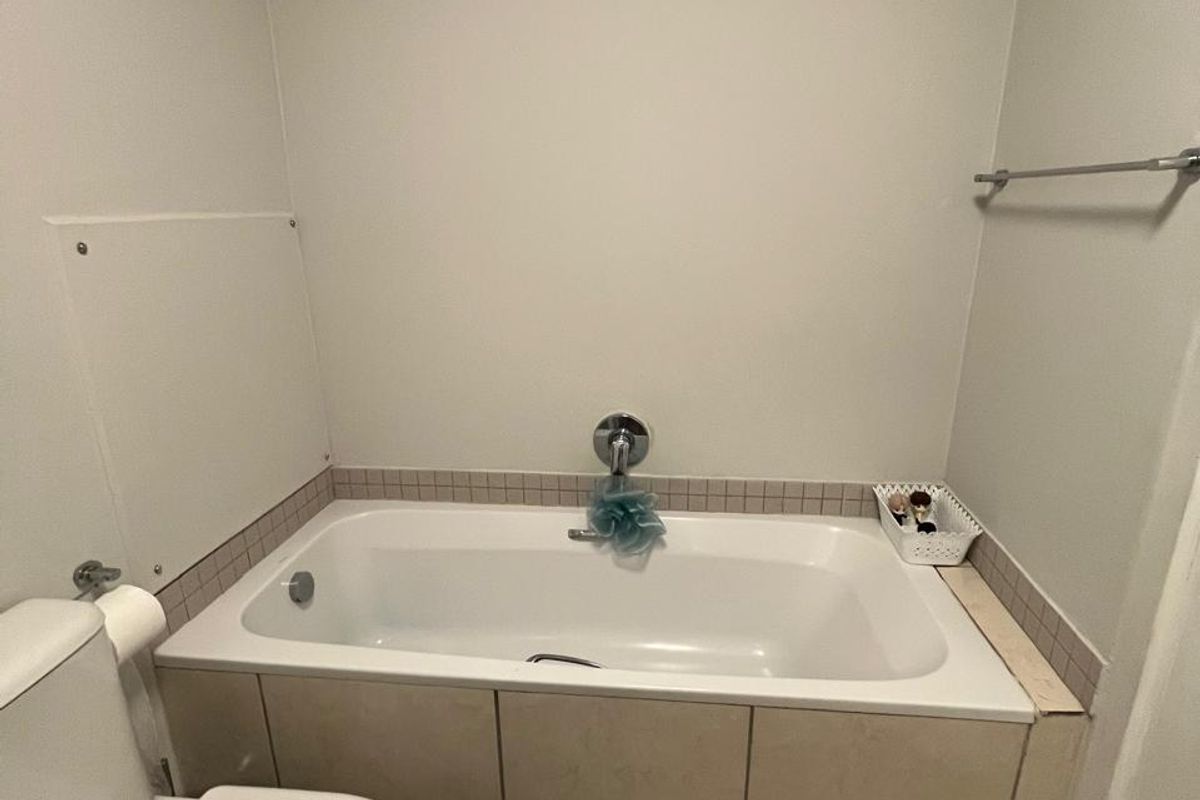 A functional bathroom featuring a built-in bathtub with tiled surround, a standard toilet, and neutral floor tiling.