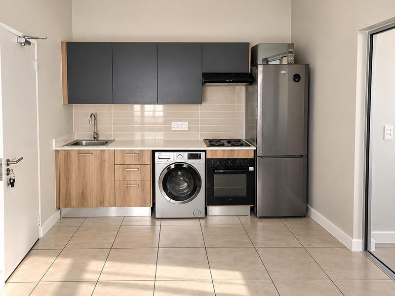 A modern, compact kitchen featuring sleek two-tone cabinetry, tiled backsplash, integrated appliances, and neutral floor tiles in a clean, well-maintained space.