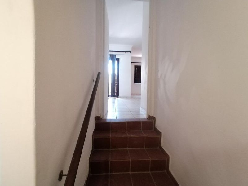 A view of a tiled staircase leading to an open living area, featuring a simple handrail and neutral wall finishes.