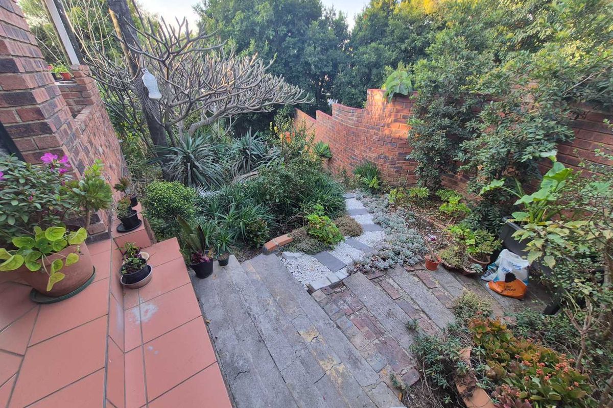 A rear garden area featuring a tiled patio, stone steps leading down to a landscaped garden, and a brick retaining wall.