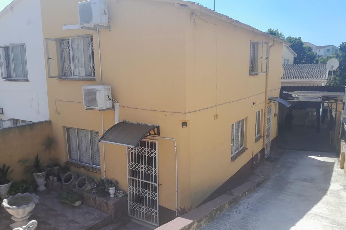 Rear exterior view of a two-story house featuring yellow painted walls, security gates, air conditioning units, and a paved patio area.