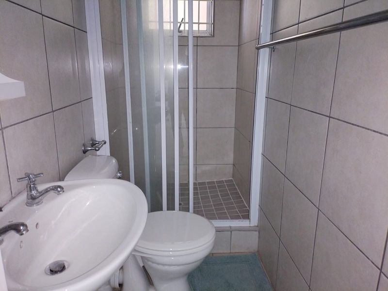 A functional bathroom featuring a shower enclosure, pedestal basin, and toilet with neutral wall tiling throughout.