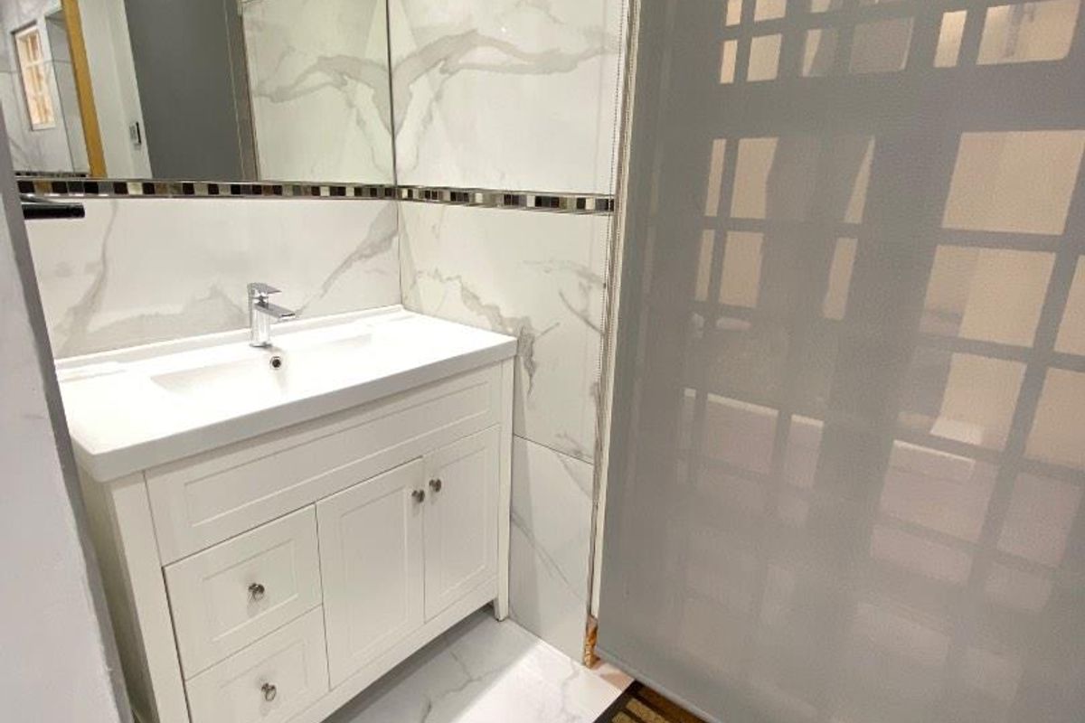 Modern bathroom featuring marble-look wall and floor tiles, a white vanity cabinet with integrated basin, and a large wall-mounted mirror.