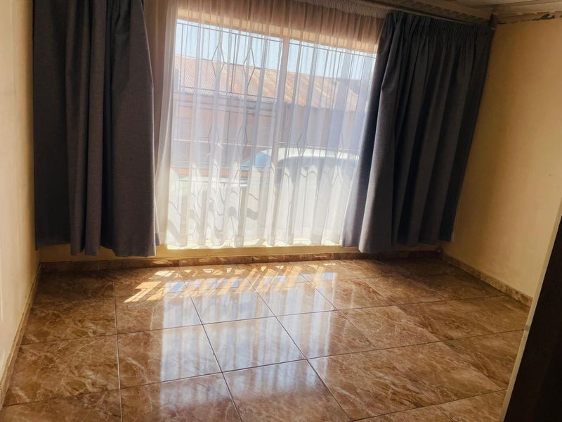 A bright, empty bedroom featuring polished marble-look floor tiles and a large window with security bars.