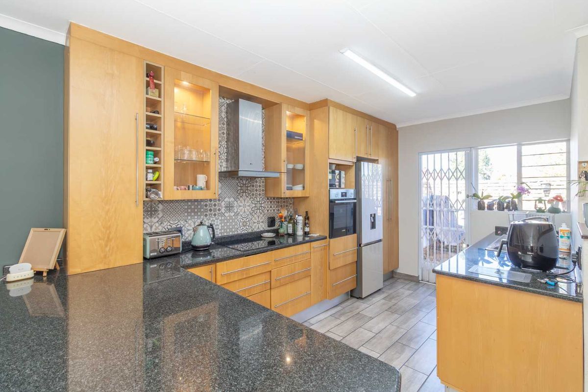 Modern kitchen featuring light wood cabinetry, granite countertops, patterned tile backsplash, built-in oven, and extractor fan with direct access to the exterior.