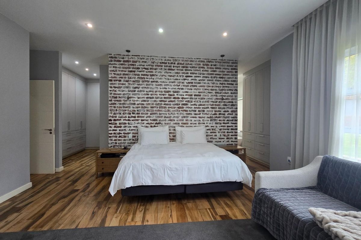 Spacious bedroom featuring an exposed brick feature wall, extensive built-in cabinetry, recessed lighting, and high-quality hardwood flooring.