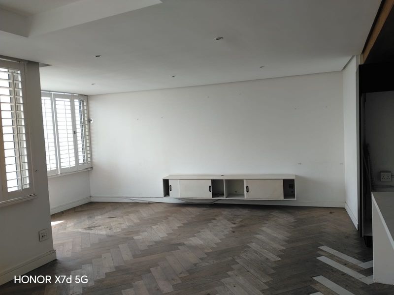 An empty living room featuring elegant herringbone timber flooring, recessed downlighting, and white plantation shutters, offering a clean canvas for interior design.