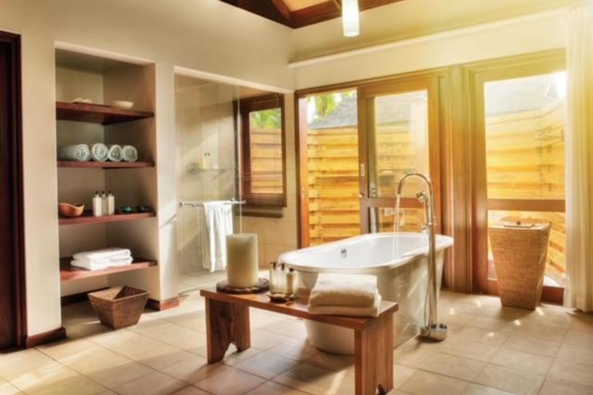 A luxurious bathroom featuring a freestanding bathtub, a glass-enclosed shower, built-in shelving, and large windows providing natural light and garden views.