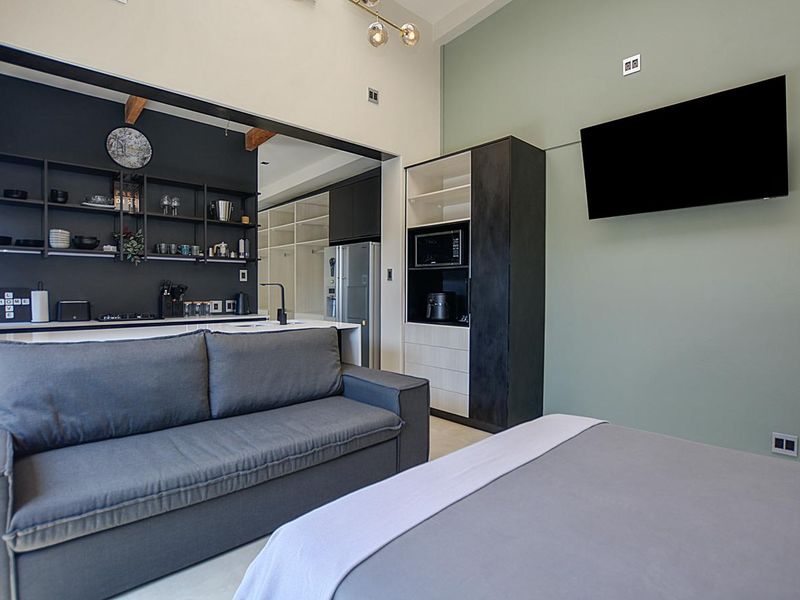 Modern open-plan apartment featuring a sleek kitchen with dark cabinetry, integrated shelving, and a functional living area with high ceilings and exposed timber beams.