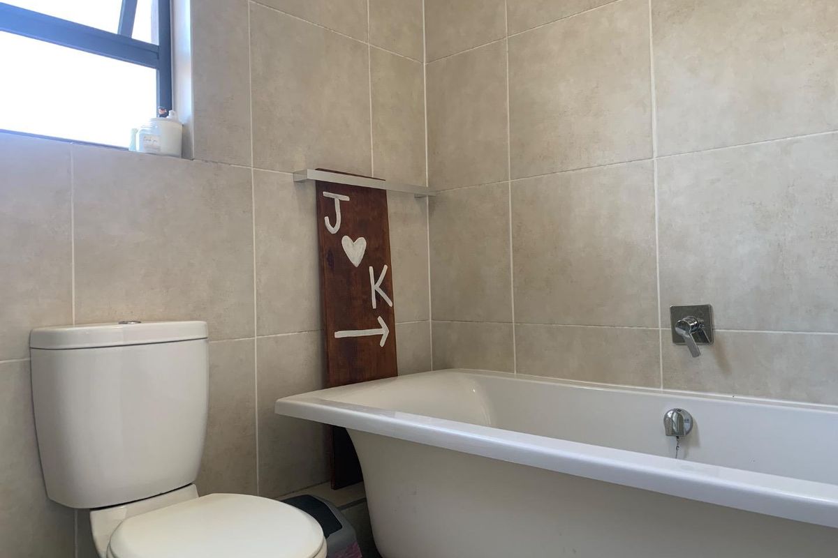 A functional bathroom featuring a white bathtub, a modern wall-mounted mixer, and a standard toilet against neutral tiled walls.