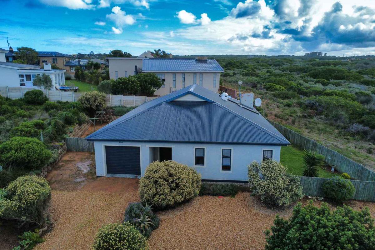 Aerial view of a detached house featuring a metal roof, single garage, and landscaped garden area with gravel driveway.