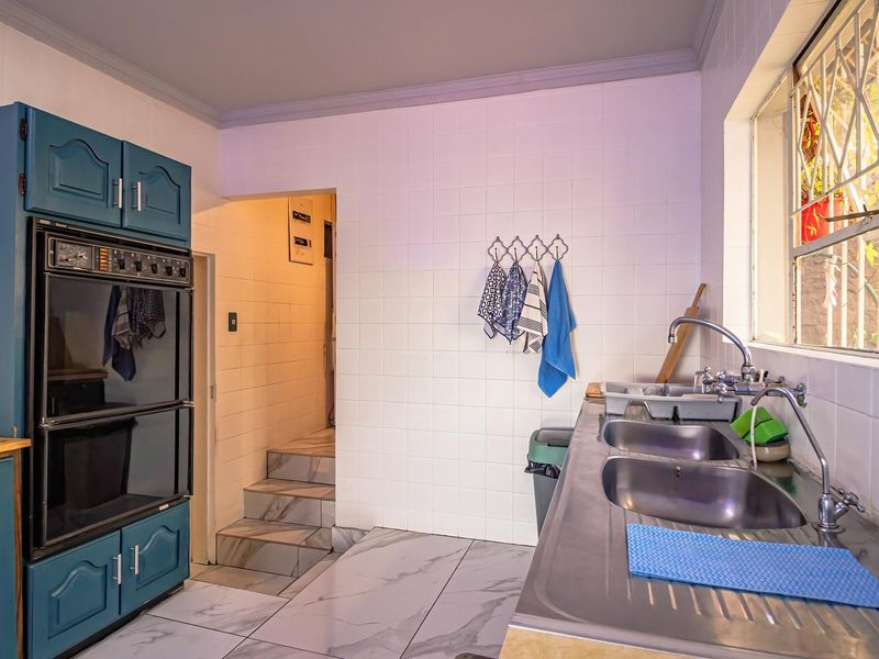 A functional kitchen featuring a built-in double oven, stainless steel double sink, and tiled finishes, offering a practical layout with direct access to adjacent areas.