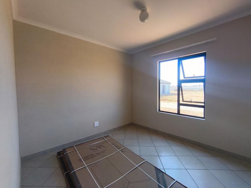 A clean, empty bedroom featuring neutral wall tones, tiled flooring, and a large aluminium-framed window providing natural light.