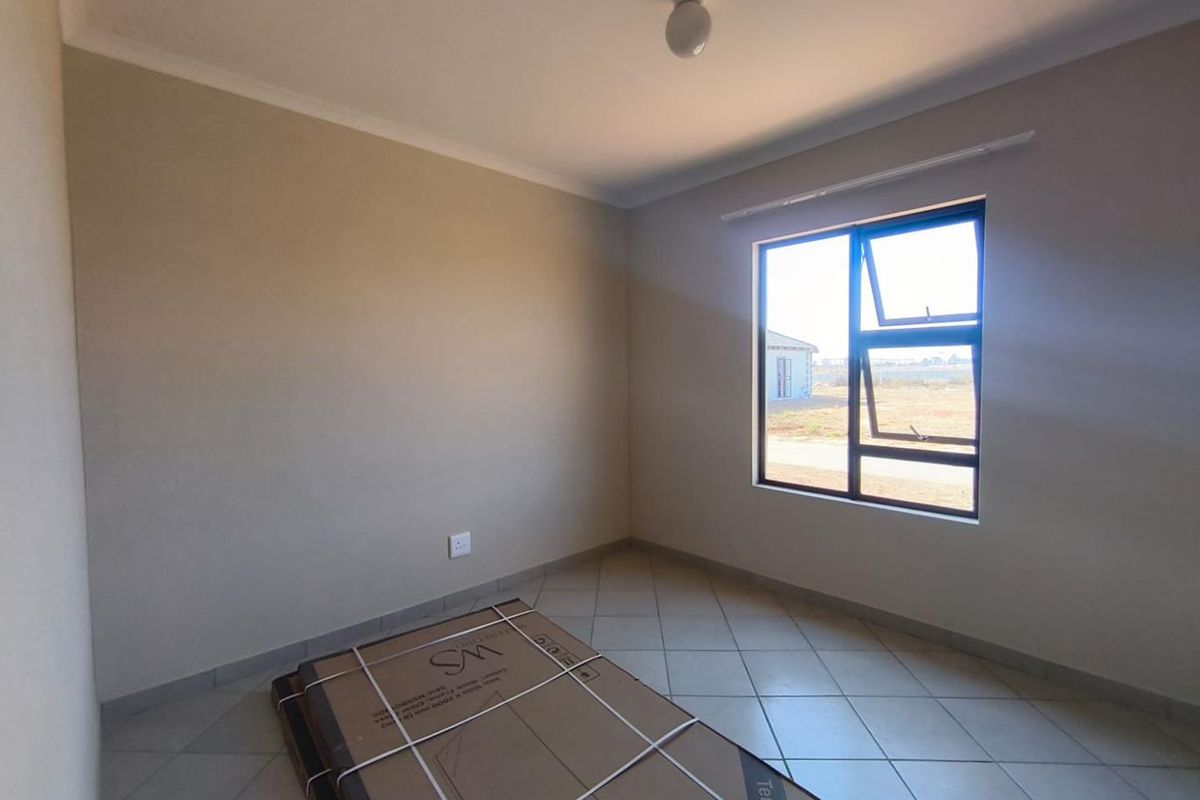 A clean, empty bedroom featuring neutral wall tones, tiled flooring, and a large aluminium-framed window providing natural light.