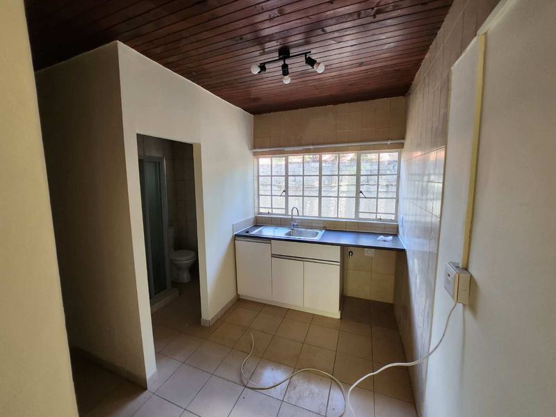 A compact, empty kitchen featuring tiled flooring, built-in cabinetry with a stainless steel sink, and a timber-paneled ceiling.