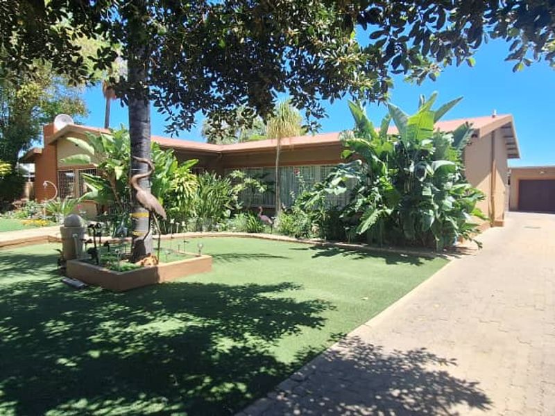 Front view of the property featuring a paved driveway, garage, perimeter wall with electric fencing, and a well-maintained garden area.