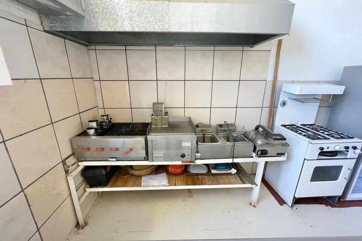 A commercial-style kitchen prep area featuring stainless steel cooking equipment, a metal extractor hood, and tiled splashbacks.