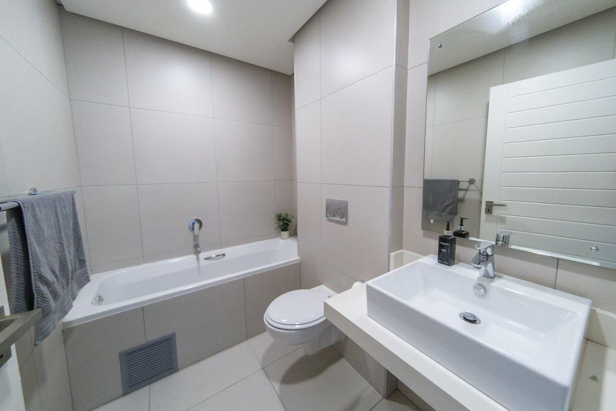 Modern bathroom featuring a built-in bathtub, wall-mounted toilet, vessel sink, and large mirror with neutral floor-to-ceiling tiling.